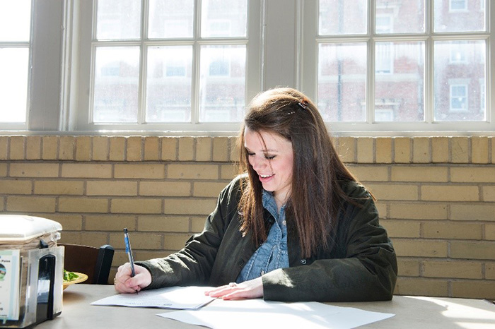 A student sitting, studying, and taking notes at a table.
