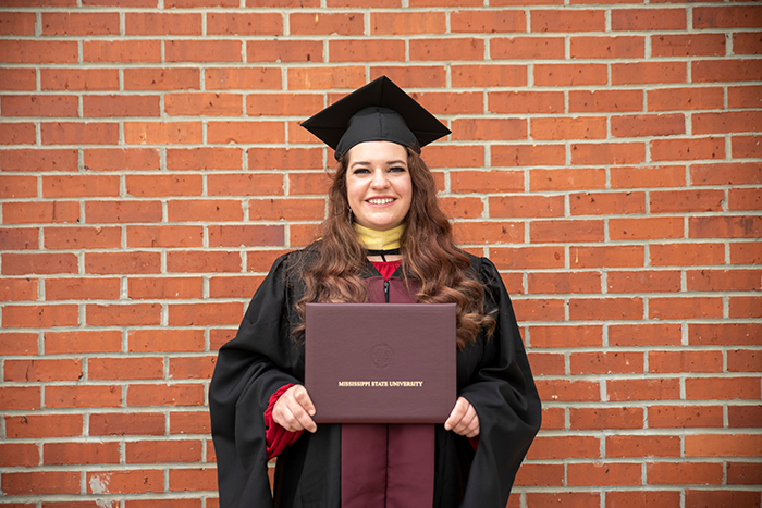 Student graduating with a bachelor’s degree from Mississippi State University holds her diploma outside Humphrey Coliseum