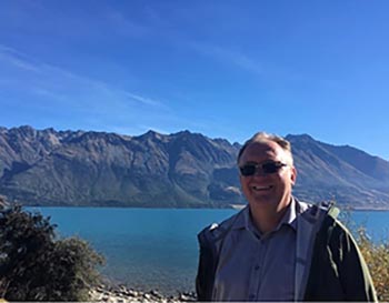 Ron Taylor standing in front of a mountain range and body of water